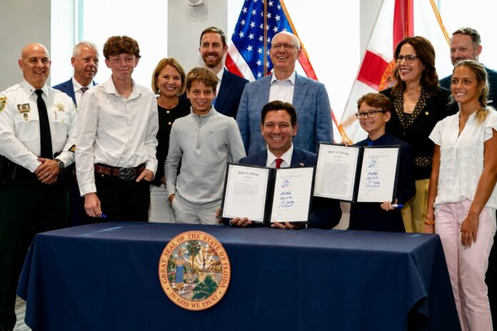 Florida Gov. Ron DeSantis holds signed budget documents while surrounded by students, educators and state officials after signing the 2026-27 Florida budget at a ceremonial event.