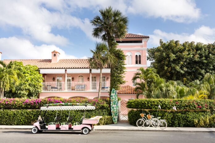 Palm Beach Buzz Weekly Edit cover for October 12–18, 2026, featuring a pink hotel surrounded by palm trees, with a pink golf cart and bicycles outside.