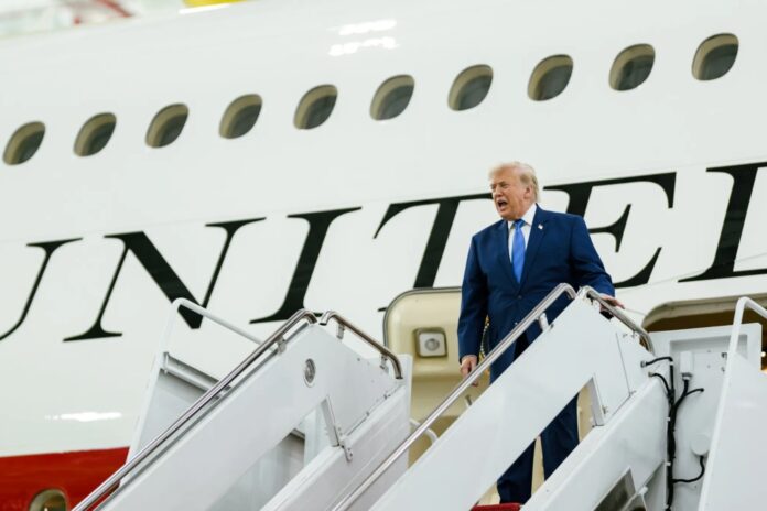 President Donald Trump stands on the stairs of his aircraft, with the United States lettering visible on the fuselage.